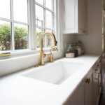 closeup of white counter top and sink in kitchen with gold sink faucet
