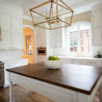 Island with brown wooden counter in large white kitchen with gold accents
